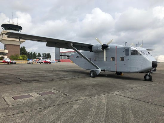 gray Short SC.7 skyvan sitting on the tarmac near a airport control tower